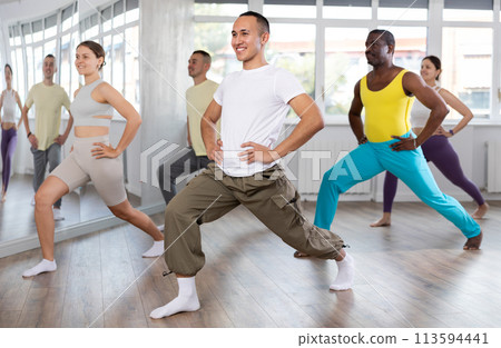 Group of young women and men in sportswear performing contemporary street dance in training room Group of young women and men in sportswear performing contemporary street dance in training room 113594441