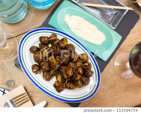 Flavored caracoles(Spanish) snails in shells, served with white sauce and red wine presented in a restaurant Flavored caracoles(Spanish) snails in shells, served with white sauce and red wine presented in a restaurant 113594754