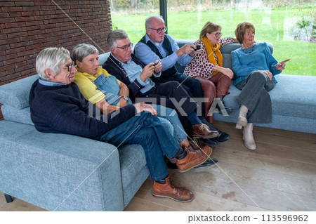 Senior Friends Engrossed in Smartphone Technology on a Couch Senior Friends Engrossed in Smartphone Technology on a Couch 113596962