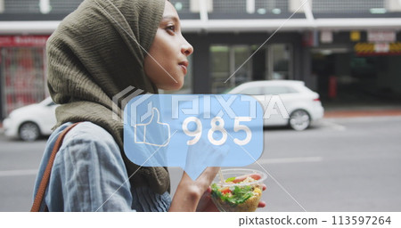 Thumbs up icon with increasing likes against woman in hijab walking on the street with a snack 113597264