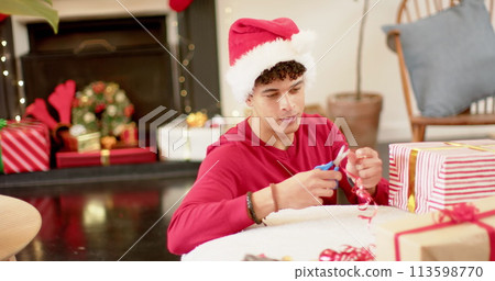 Young biracial man wrapping gifts at home, with copy space 113598770