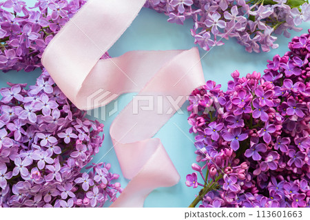 product advertising backdrop. Lilac blooming flowers and pink ribbon on blue background with copy space for text or beauty product. Top view, flat lay, flower frame or border, spring summer 113601663