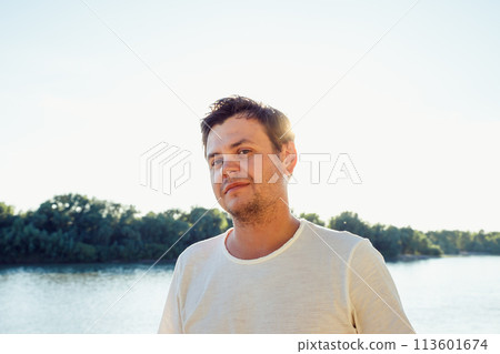 young adult man looking at camera on lake. Positive emotions, leisure activity, hiking, relax and vacation in summer. lifestyle male portrait 113601674