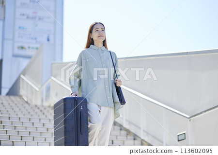 Female inbound foreign traveler walking down the stairs with a suitcase 113602095