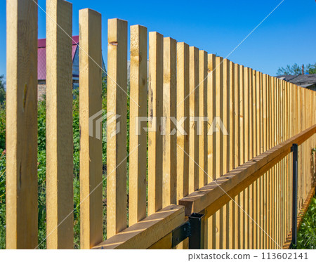 Close-up of a new wooden picket fence in the backyard of a country house, a sunny summer day 113602141