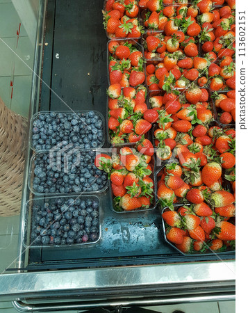 Lots of blueberries and strawberries in containers on the counter in the store, close-up, vertical 113602151