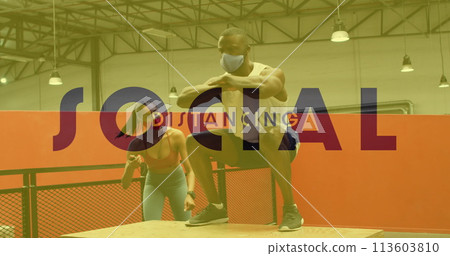 Social distancing text against african american man wearing face mask jumping on plyo box at gym 113603810