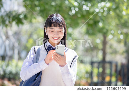 A high school girl wearing earphones and looking at her smartphone A high school girl wearing earphones and looking at her smartphone 113605699