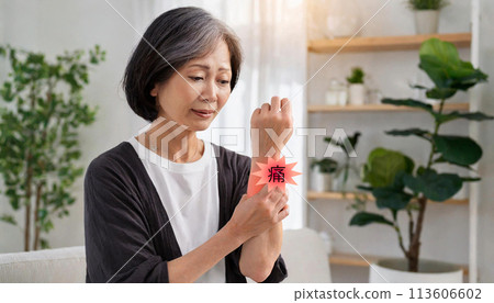 An elderly woman suffering from pain in her wrist, holding it with her other hand. 113606602