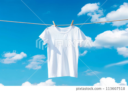 White t-shirt hanging on clothesline against blue sky with clouds 113607518
