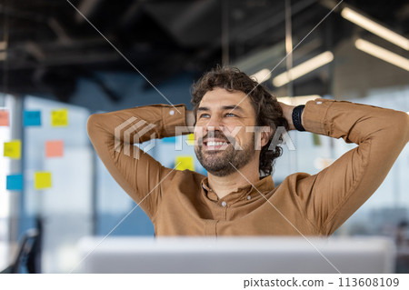 A mature Hispanic man exhibits a content smile, resting at his workplace with a confident posture. 113608109