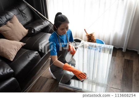 Cleaning service worker in wearing rubber gloves wiping the dust off glass table in living room 113608254