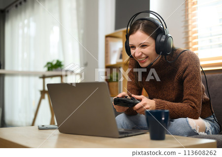 Young caucasian woman in headset holding joystick playing video game on laptop Young caucasian woman in headset holding joystick playing video game on laptop 113608262