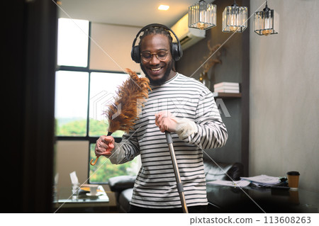 Happy African American man having fun cleaning house and singing using duster as microphone. 113608263