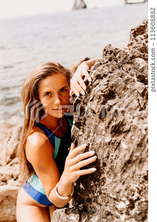 Woman beach vacation photo. A happy tourist in a blue bikini enjoying the scenic view of the sea and volcanic mountains while taking pictures to capture the memories of her travel adventure. Woman beach vacation photo. A happy tourist in a blue bikini enjoying the scenic view of the sea and volcanic mountains while taking pictures to capture the memories of her travel adventure. 113608882