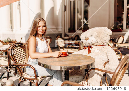 A woman sits cafe with a teddy bear next to her. The scene is set in a city with several chairs and tables around her. The woman is enjoying her time at the outdoor cafe. A woman sits cafe with a teddy bear next to her. The scene is set in a city with several chairs and tables around her. The woman is enjoying her time at the outdoor cafe. 113608948