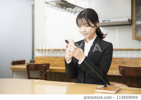 A young woman in a business suit using a smartphone in a cafe 113609009