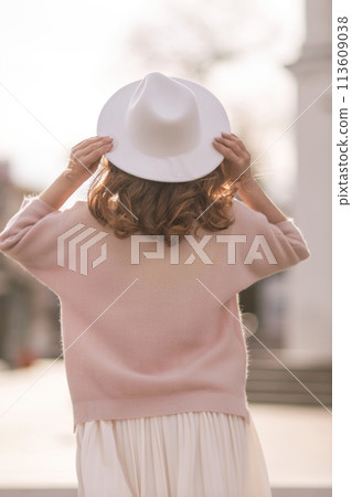 A woman wearing a white hat and a pink sweater stands in front of a building A woman wearing a white hat and a pink sweater stands in front of a building 113609038