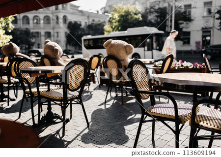 A restaurant with a lot of chairs and tables. There are two teddy bears on the tables. 113609194