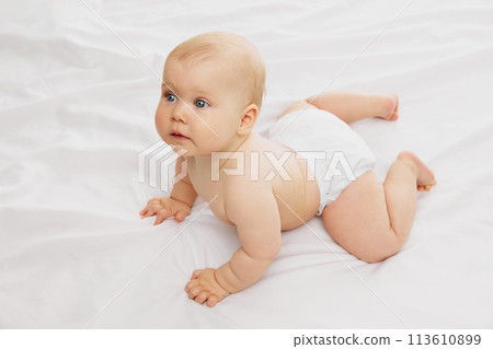 Serene, cute baby in diaper, rests on textured white fabric on bed embodying the calmness of early childhood. Serene, cute baby in diaper, rests on textured white fabric on bed embodying the calmness of early childhood. 113610899