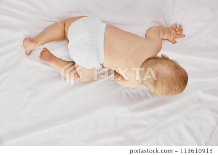 Aerial view photo of little charming baby lies on belly, on comfy, soft bed covered with white fabric. Cute explorer. Aerial view photo of little charming baby lies on belly, on comfy, soft bed covered with white fabric. Cute explorer. 113610913