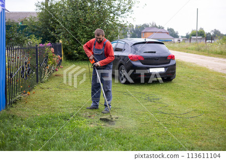 A man mows the grass in front of his house with a lawnmower. A man mows the grass on his lawn with an electric lawn mower. Lawn care and grass cutting with a lawn mower. 113611104