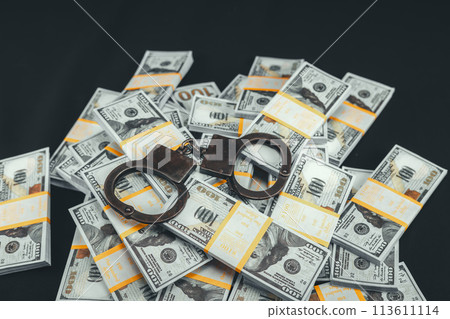 Hundred dollar bills scattered on a black background and dark handcuffs lying on them. Money is piled up in a heap on a black background, with handcuffs on top of them. 113611114