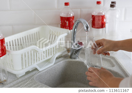 Washing plastic bottles for recycling. At home in the kitchen, a woman rinses plastic bottles with water and collects them for recycling. Sorting household waste for recycling. 113611167
