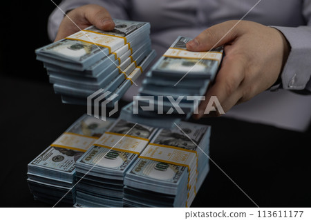 Folding money into piles on a black background. Close-up. A man carefully puts money in piles on a black background. A lot of money in packed bundles. Folding money into piles on a black background. Close-up. A man carefully puts money in piles on a black background. A lot of money in packed bundles. 113611177