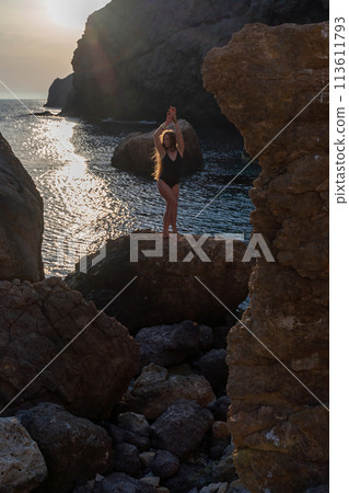 Woman tourist enjoying the sunset over the sea mountain landscape. Sits outdoors on a rock above the sea. She is wearing jeans and a blue hoodie. Healthy lifestyle, harmony and meditation Woman tourist enjoying the sunset over the sea mountain landscape. Sits outdoors on a rock above the sea. She is wearing jeans and a blue hoodie. Healthy lifestyle, harmony and meditation 113611793