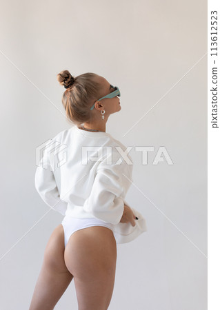 Beautiful blonde girl in a hoodie and panties posing with her back on a white background 113612523