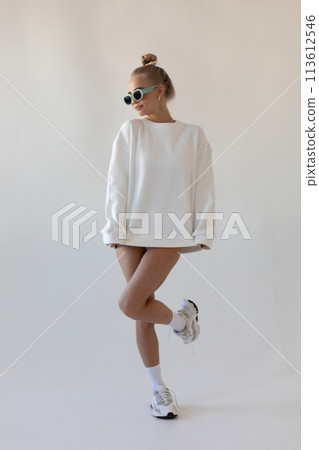 Beautiful blonde girl in a hoodie and panties posing with her back on a white background 113612546