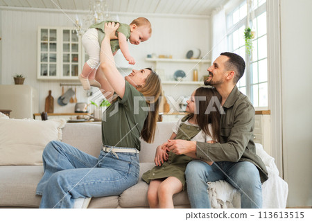 Happy family at home. Mother father two children daughters relaxing on sofa indoor. Mom dad parents baby girls kids relax playing having fun together. Family smiling laughing enjoying tender moment 113613515