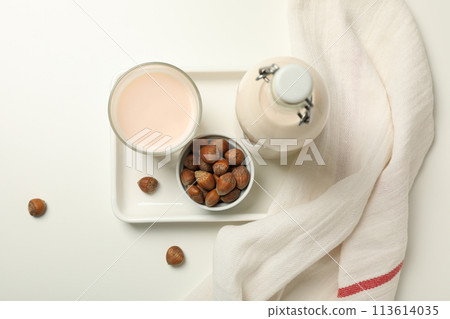 Bottle and glass with milk, towel and bowl with nuts on white background, top view 113614035