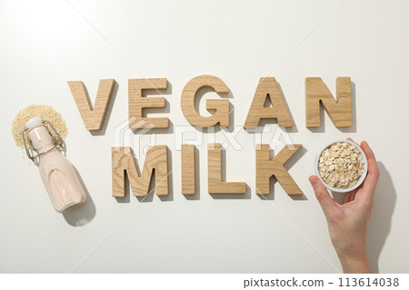 Bottle with milk, sesame seeds, oatmeal in bowl and hand, wooden letters on white background, top view Bottle with milk, sesame seeds, oatmeal in bowl and hand, wooden letters on white background, top view 113614038