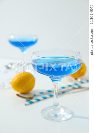 Blue cocktail in glass, whole lemon, straws and ice cubes on white background Blue cocktail in glass, whole lemon, straws and ice cubes on white background 113614043