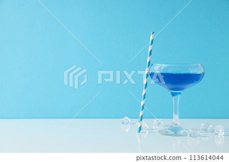 Blue cocktail in glass, straw and ice cubes on blue background, space for text Blue cocktail in glass, straw and ice cubes on blue background, space for text 113614044