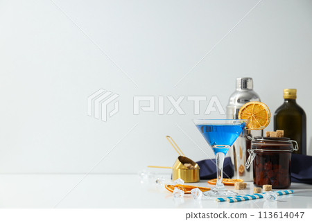 Blue cocktail in glass, oranges slices, bottles and ice cubes on white background, space for text 113614047