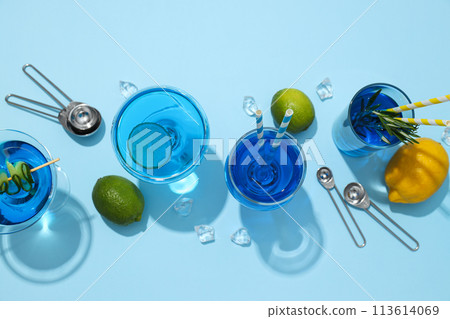 Blue drink in cocktail glasses, lemons, limes and ice cubes on blue background, top view Blue drink in cocktail glasses, lemons, limes and ice cubes on blue background, top view 113614069