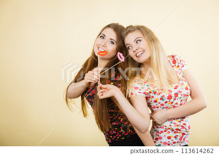 Two happy women holding fake lips on stick 113614262