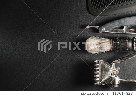 On a black surface are old barber tools.Two vintage manual hair clipper, comb, razor, shaving brush. black monochrome. Horizontal orientation. Top view, flat lay. copy space On a black surface are old barber tools.Two vintage manual hair clipper, comb, razor, shaving brush. black monochrome. Horizontal orientation. Top view, flat lay. copy space 113614828