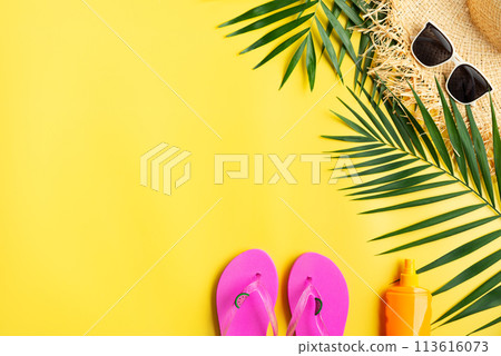 Vacation travel planning simple theme of straw hat sunglasses flip flops and palm leaves on uniform yellow background flat lay with copy-space 113616073