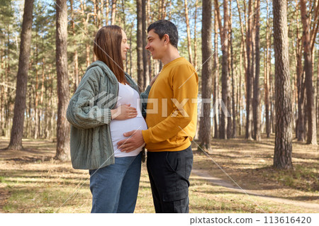 Loving pregnant woman and man walking in spring forest enjoying positive moments future father embracing big belly looking with love at her wife expectant parents walking in park Loving pregnant woman and man walking in spring forest enjoying positive moments future father embracing big belly looking with love at her wife expectant parents walking in park 113616420