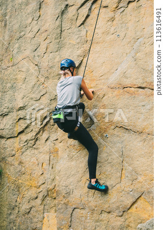 Young athletic woman in equipment doing rock climbing outdoors. Training area for outdoor activities. Extreme sport. 113616491