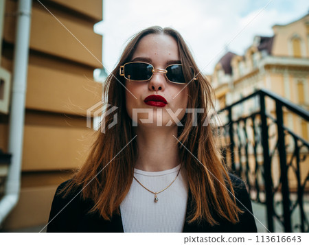 A woman in sunglasses, a white shirt and a black jacket stands confidently on the street. A woman in sunglasses, a white shirt and a black jacket stands confidently on the street. 113616643