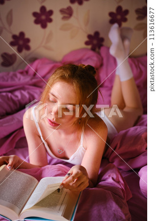 Pretty redhead Girl qith blue eyes and red hairs In White underwear Reads Book lie On pink bed 113616677