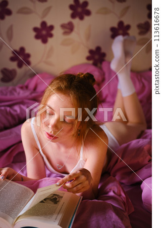 Pretty redhead Girl qith blue eyes and red hairs In White underwear Reads Book lie On pink bed 113616678