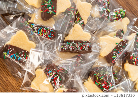 Carefully packaging Christmas cutout cookies, half-dipped in chocolate and presented in clear cellophane wrapping, perfect for festive gifting. Carefully packaging Christmas cutout cookies, half-dipped in chocolate and presented in clear cellophane wrapping, perfect for festive gifting. 113617330