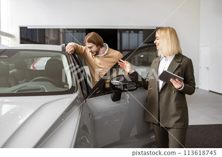 Female car dealer standing with client of dealership in showroom. Female car dealer standing with client of dealership in showroom. 113618745