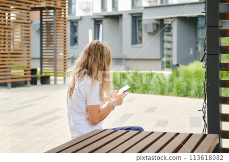 Unrecognizable woman in sunglasses on bench with smartphone 113618982